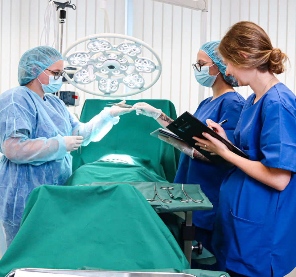 The picture shows our Medical UX Lab. Three employees are standing around an operating table in the usability and UX lab testing a medical device.