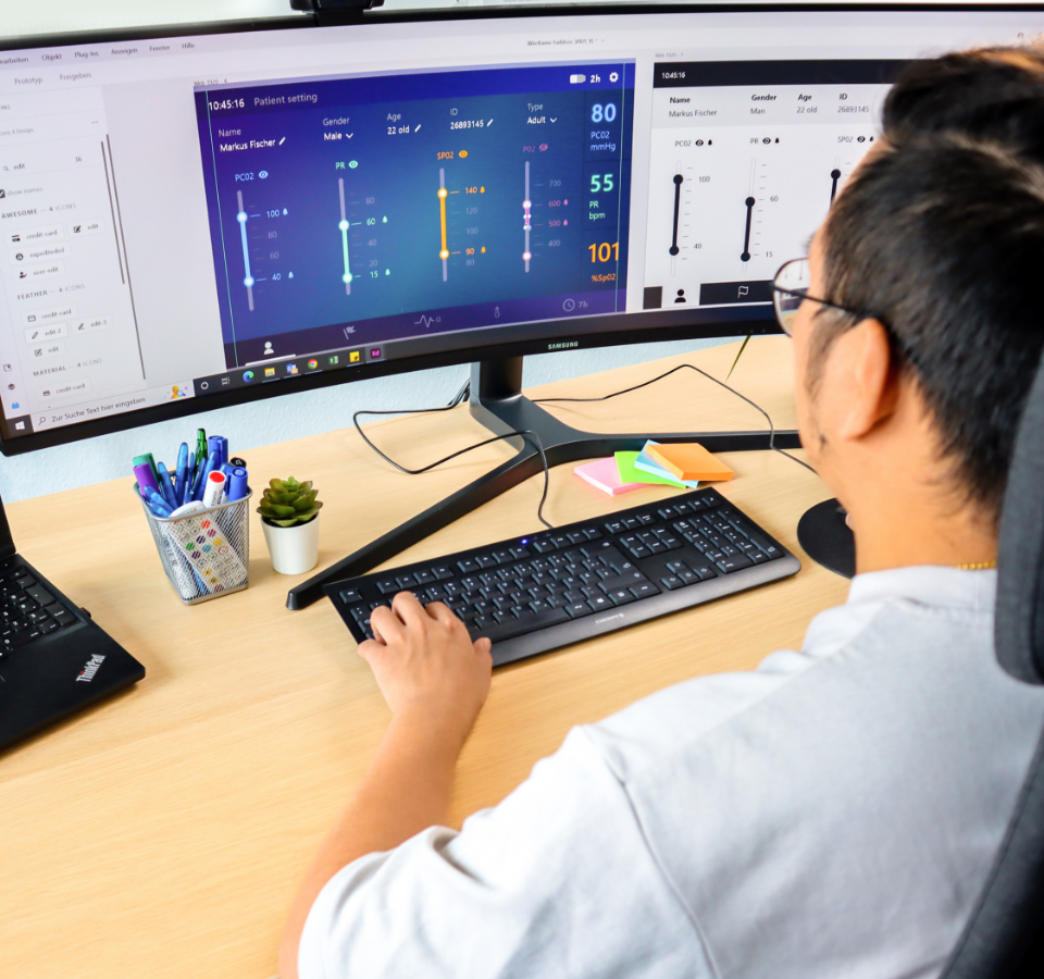 This picture shows a Custom Medical employee from behind. He is sitting at the computer.