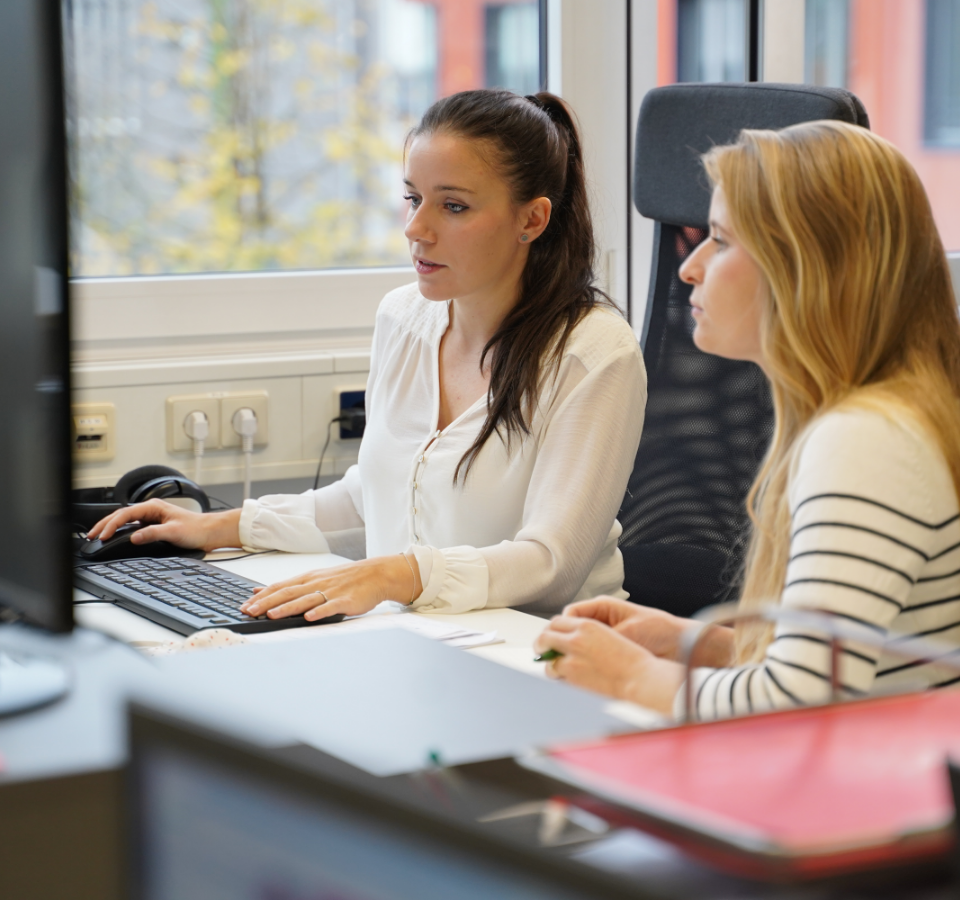 Two female employees in front of a computer screen plan initial measures for a project.