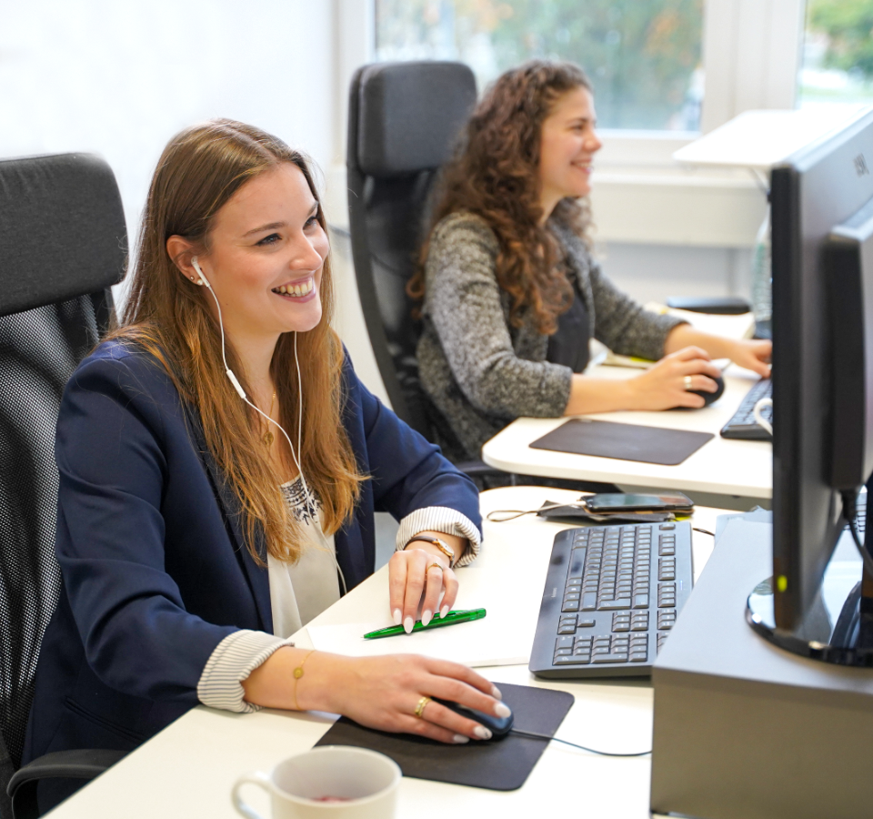 Two colleagues sit smiling at their workstations.